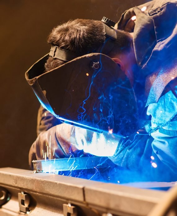 Young man with protective mask welding in a factory